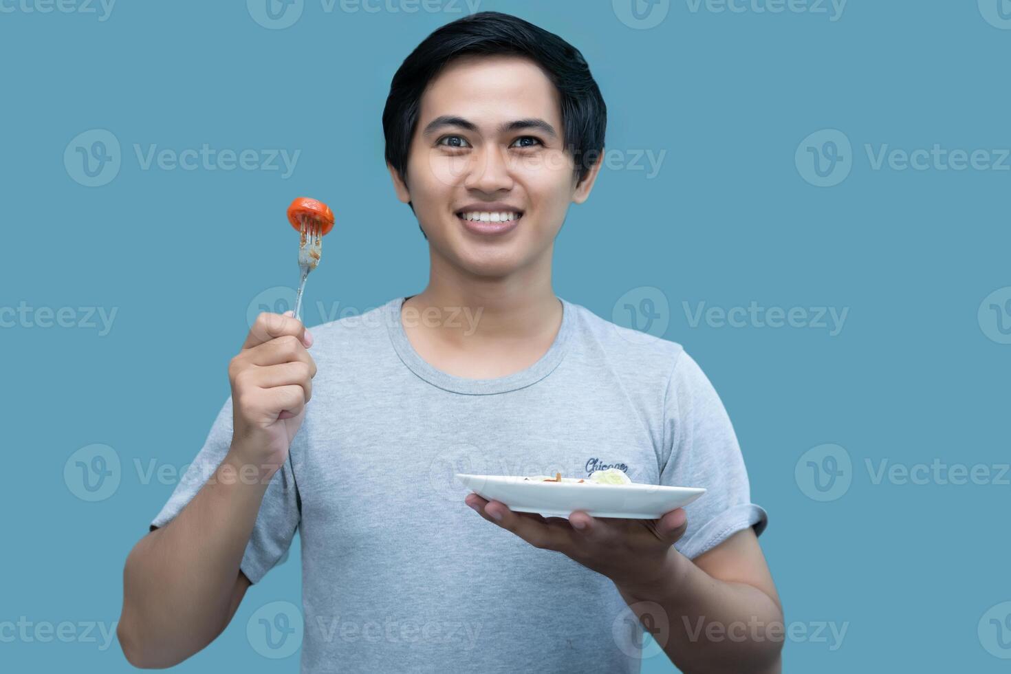 A man in a gray shirt is holding a fork and a plate containing food, for design and visual editing purposes. photo