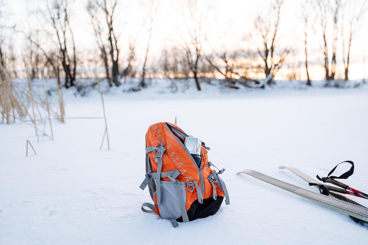 An orange backpack stands on the snow, cross-country skis lie nearby. Countryside scenery. Active lifestyle. photo