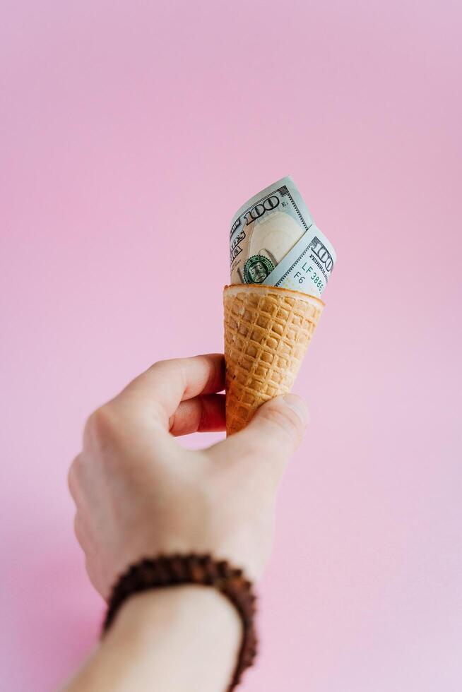 In hands is ice cream cone with a hundred dollars. Instead of cream in the cone rolled up a thousand dollars.unusual abstract photo with money and food.