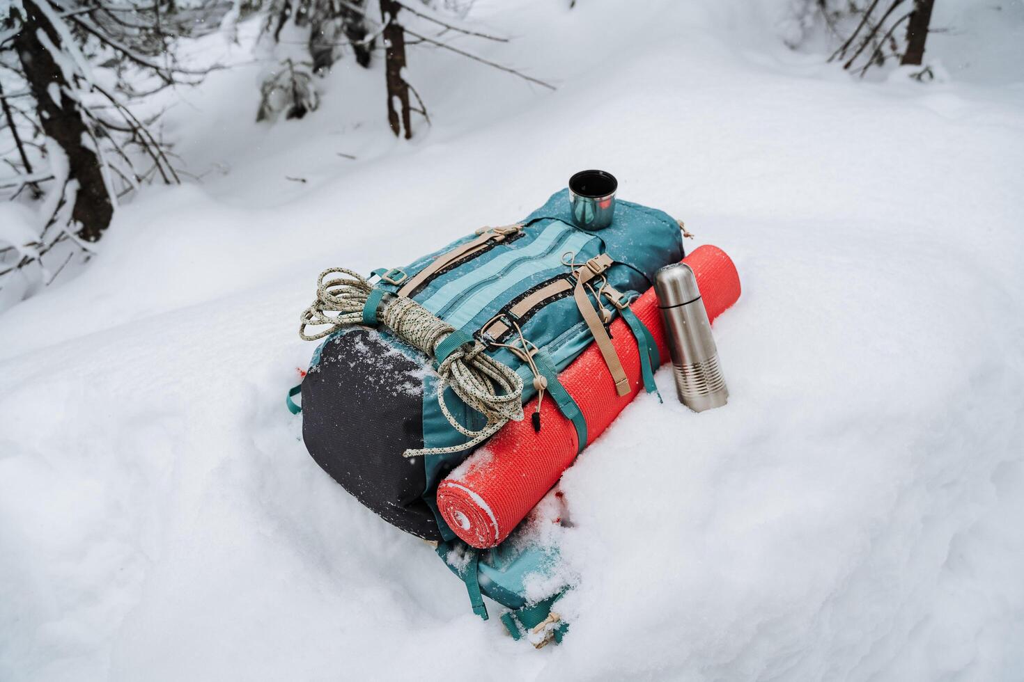 A backpack with camping gear lies on the snow. Winter hike in the mountains, equipment for climbing. Thermos with tea. photo