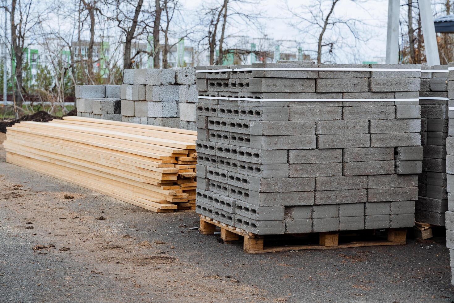 Concrete blocks are stacked in even rows, a warehouse of building materials in the open air, boards lie in a heap on the ground, flat bricks for building a house. photo