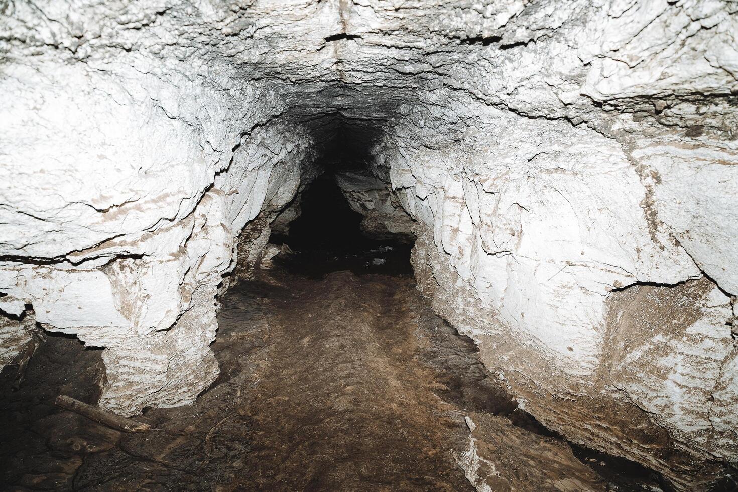 Speleology hike to the cave, lantern illuminates the underground abyss karst formation, lime cave, passage dirty bottom clay. photo