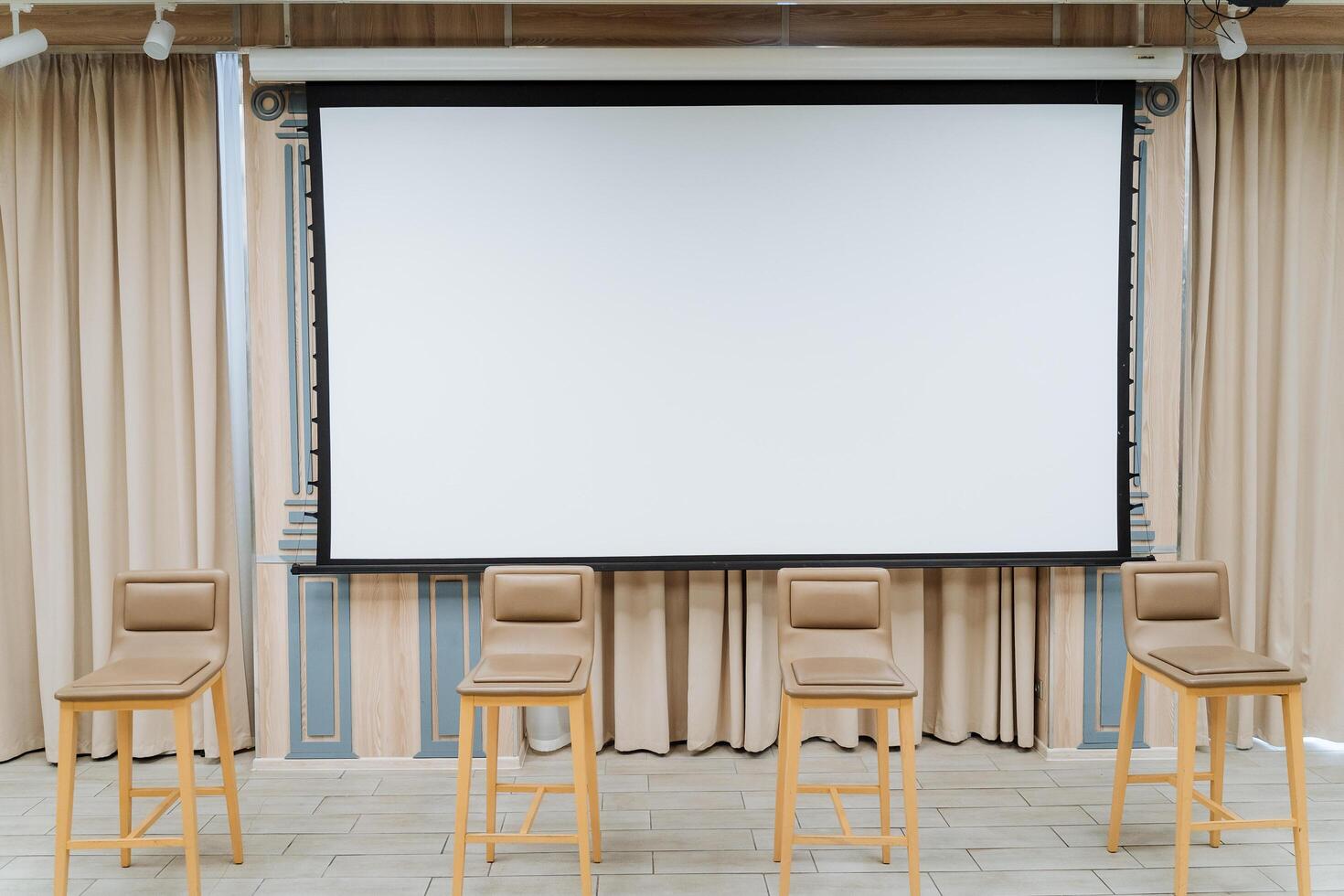 A white screen for showing the video hangs on the wall. Four chairs stand on the stage. Conference hall, business class for performances. photo