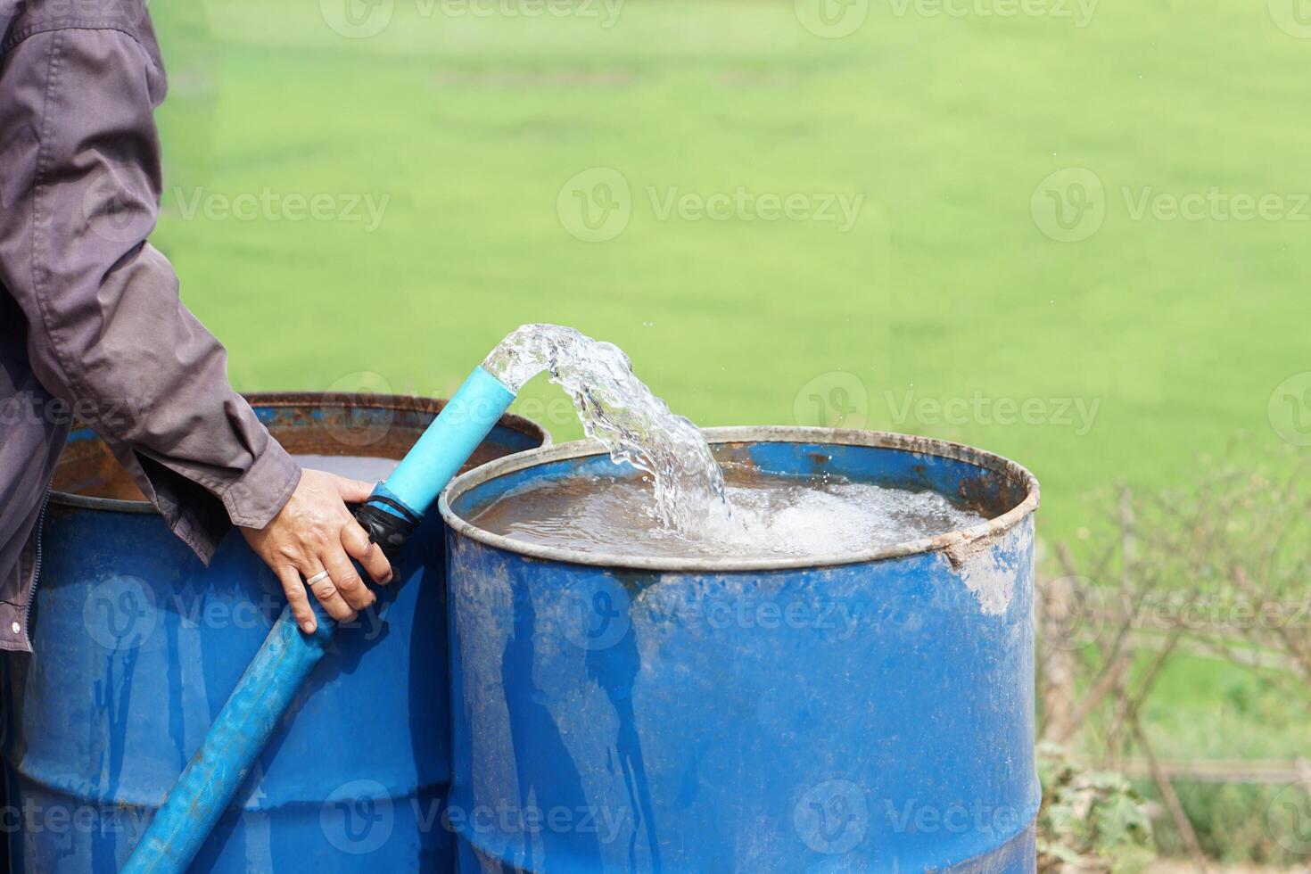 cerca arriba granjero mano sostener tubo de agua a poner dentro azul cubos en jardín. concepto, resolver problemas carente de agua en agricultura por preparar agua para riego plantas en sequía estación. foto