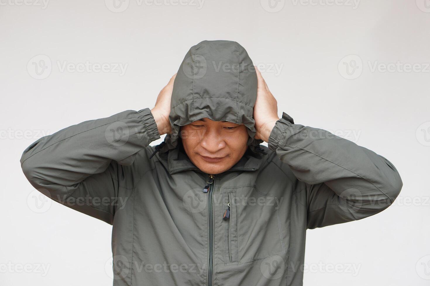 Asian man wears hoodie, uses his hands to cover ears. Concept, don't want to listen or hear anything. Distressed by noise. Avoid listening to noise of complains or negative words. photo