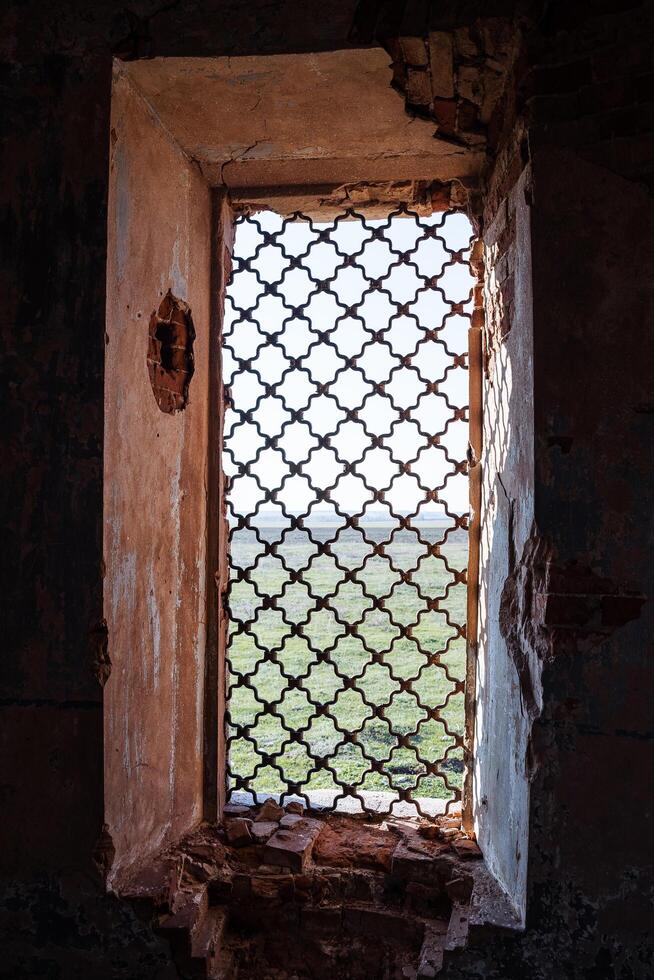 The window of the old building is covered with a forged lattice, sunlight illuminates the walls of the ancient temple, the old church window to the street, the metal lattice of cast iron photo