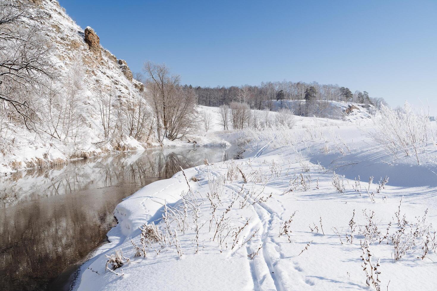 The river flows along the rock of the banks covered with snow. Winter landscape, cold season frosty weather, sunny day, blue sky. photo