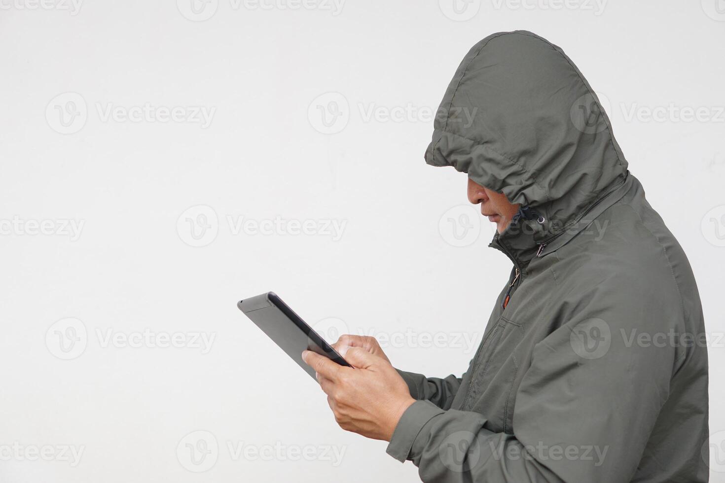 Man hacker wears hoodie, holds smart tablet. Concept, digital information security, Cyber security. Online Criminal. Man is checking and searching information from internet. photo