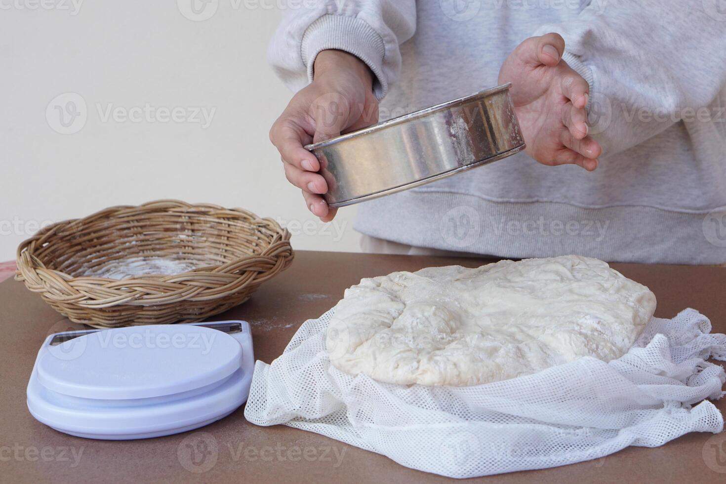 Closeup hand holds colander, dough flour for making bread or pizza, basket, scale on cookng table. Concept, cooking. Kitchen lifestyle. Preparing food. Bakery. Love cooking photo