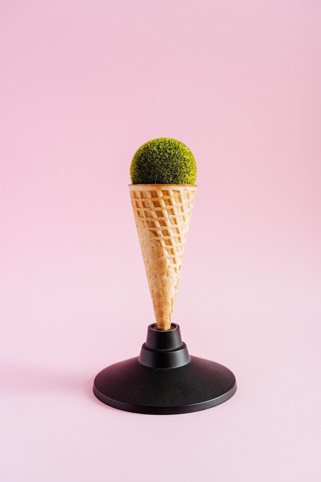 A waffle ice cream cone is on a plastic stand. An unusual shot of food. Instead of ice cream, the sphere is made of lawn. Green Food photo