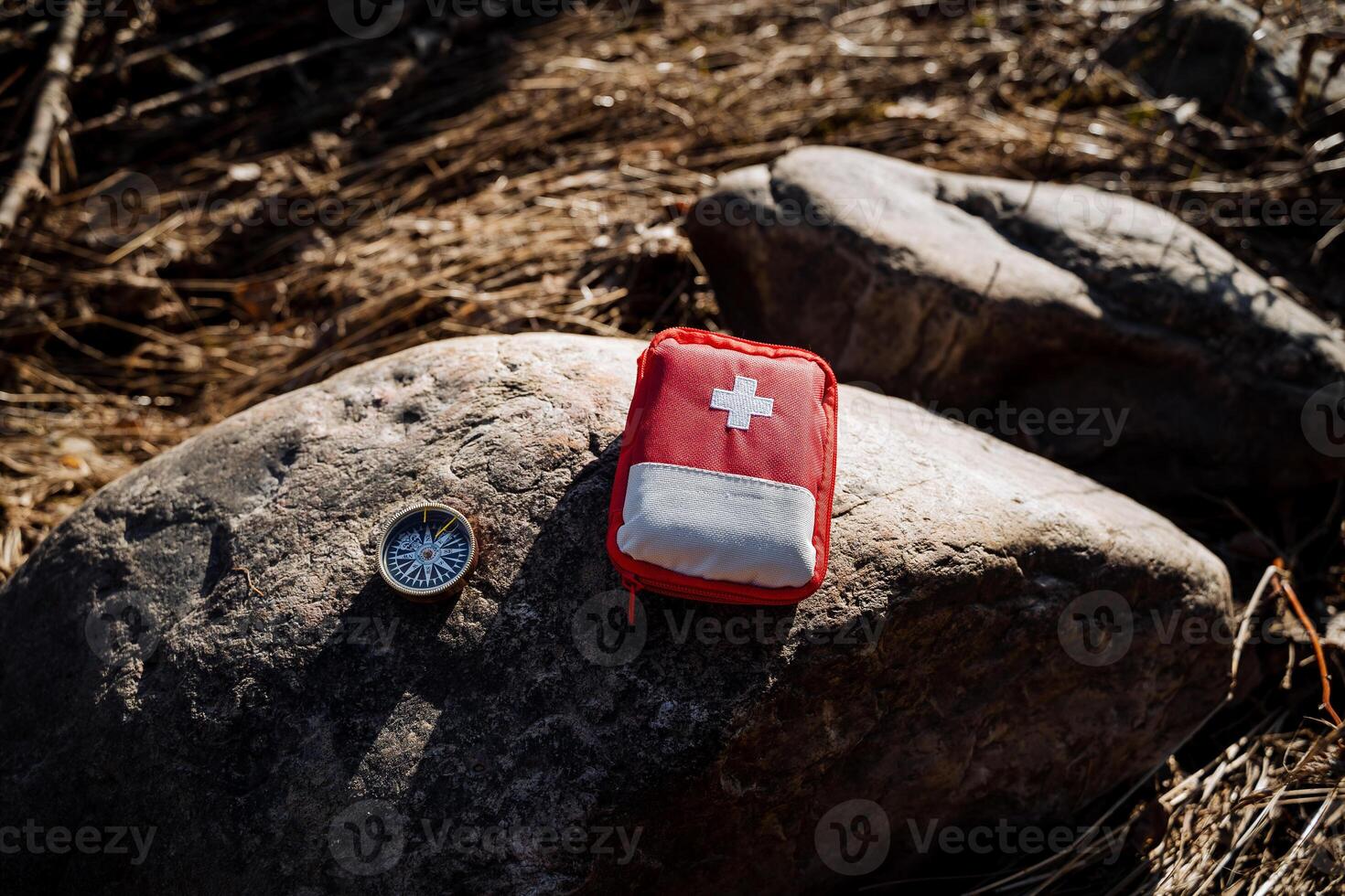 A red first aid kit bag lies on a stone, a compass for emergency rescue, basic necessities in a hike in the forest. photo