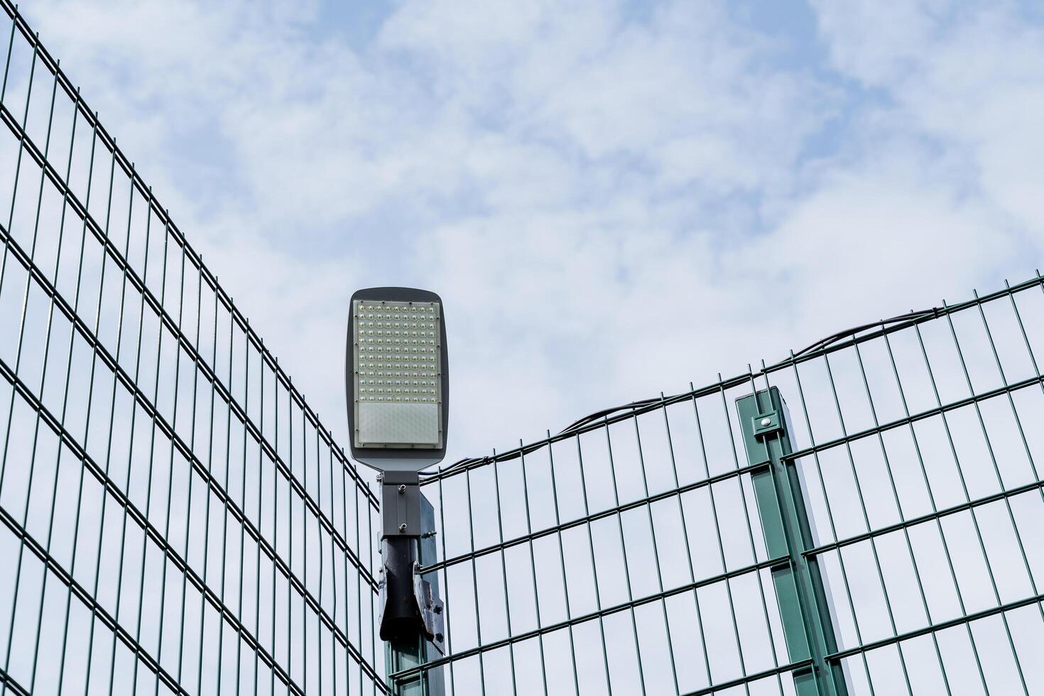 LED street lamp hanging on the fence, modern lighting of sports grounds, energy saving new technologies, lamp during the day against the sky photo