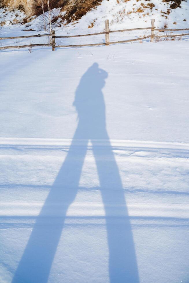 The shadow of a man in the snow, the black silhouette of the figure of a man in winter on a white background, a tourist walks through the forest casting a shadow. art fragment photo