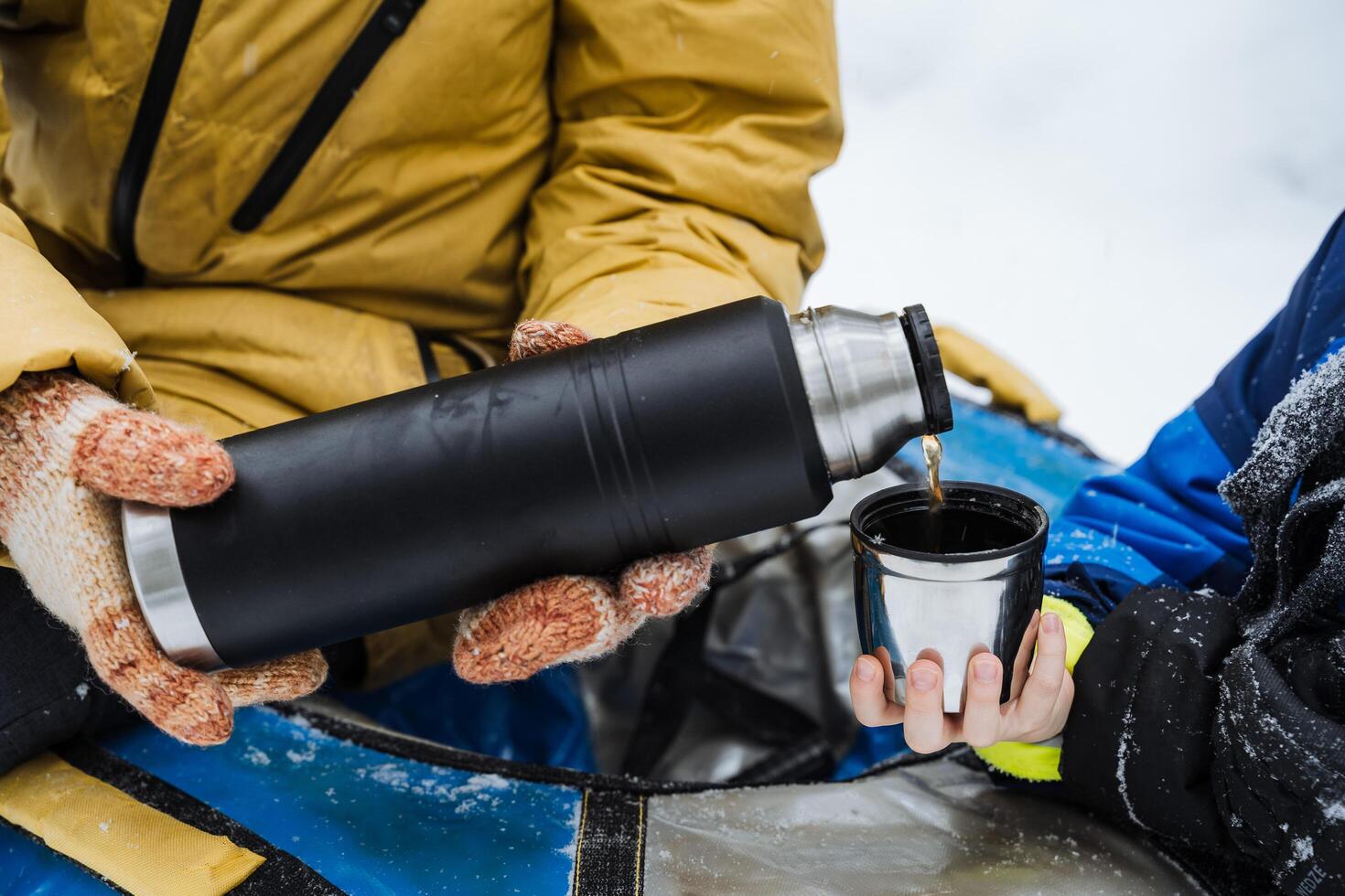 Steel thermos in hand. Pour a hot drink into a mug. A glass in his hand with water. Bask in an herbal drink from a thermo bottle. Winter hike in the woods. photo