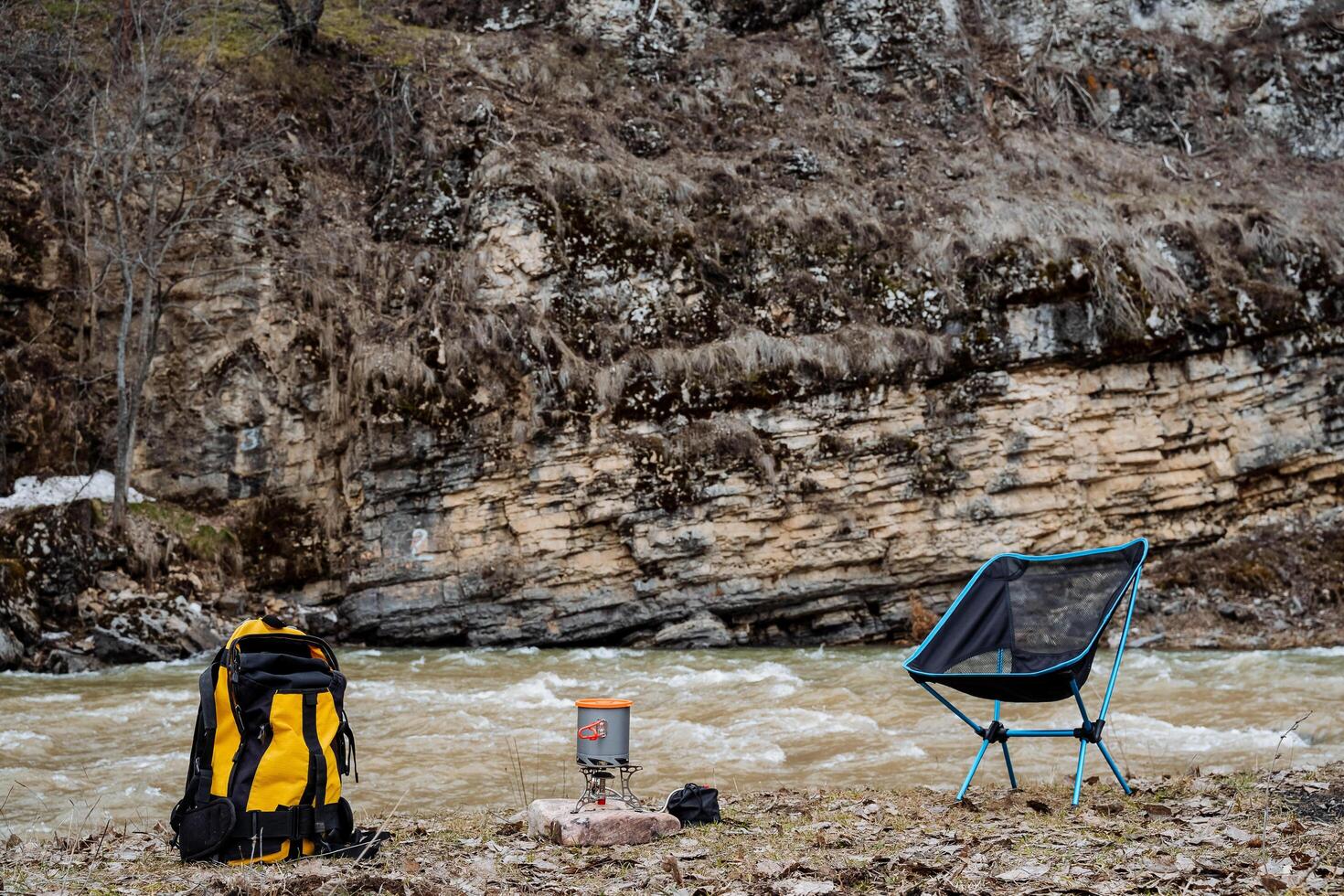 Camping on the river bank, a yellow backpack with hiking equipment, a pot on a gas burner, a folding chair for rest, a camping place. photo