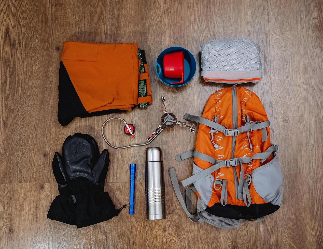 Hiking equipment, backpack, pants, thermos, mittens, lantern, windbreaker lie on the floor. Top view of the tourist equipment. Flatley. photo