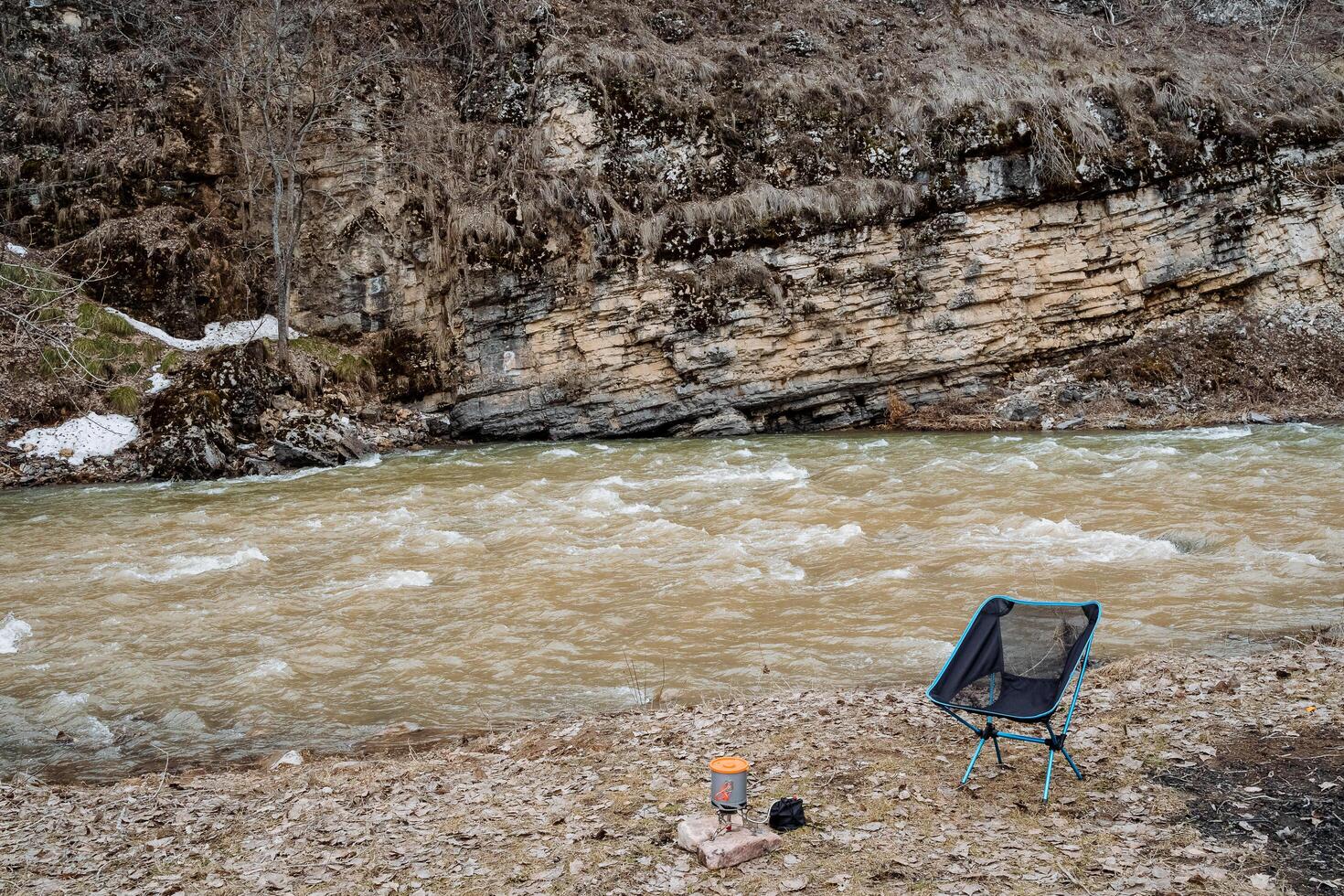 A folding chair stands alone on the bank of the river. Camping equipment. Folding chair. photo