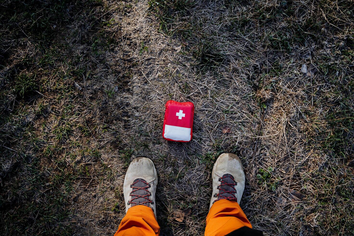 First aid kit lies on the ground at the feet, top view red bag of medicines, camping equipment, hiking, survival in the forest, cross white, photo