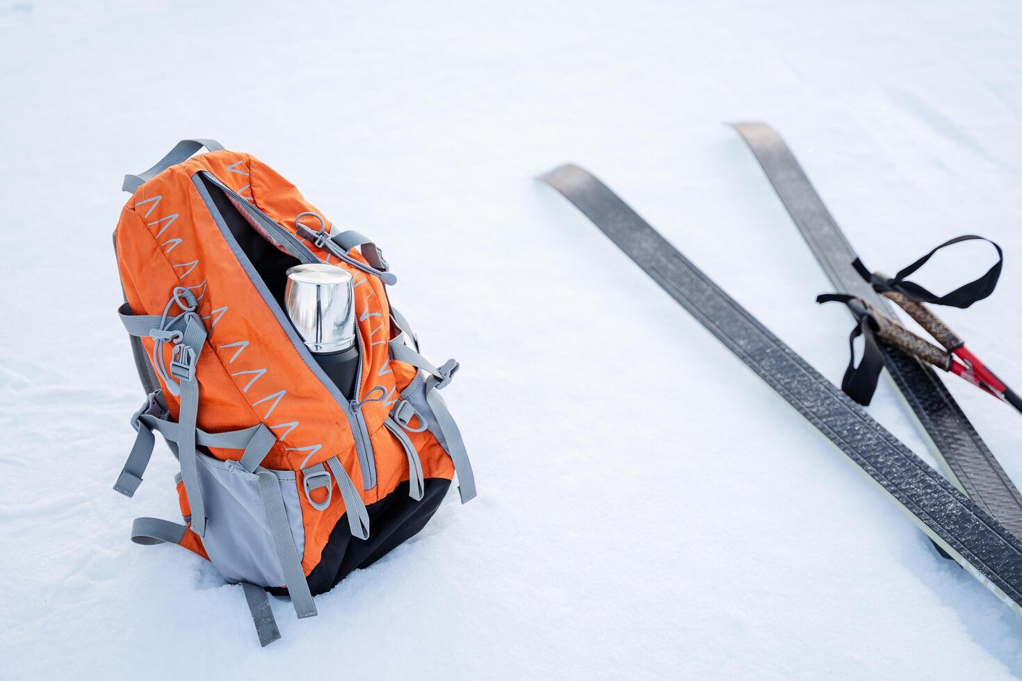 The skier stopped for lunch. The backpack lies on the snow next to a pair of skis and poles. Thermos with tea for a snack. Camping equipment for a winter hike. photo