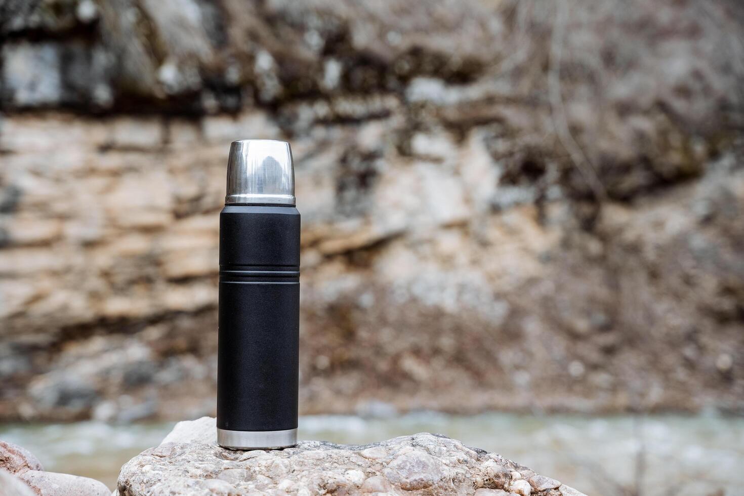 Thermos black vacuum stands on the background of a rock, a thermal bottle for hot drinks. photo