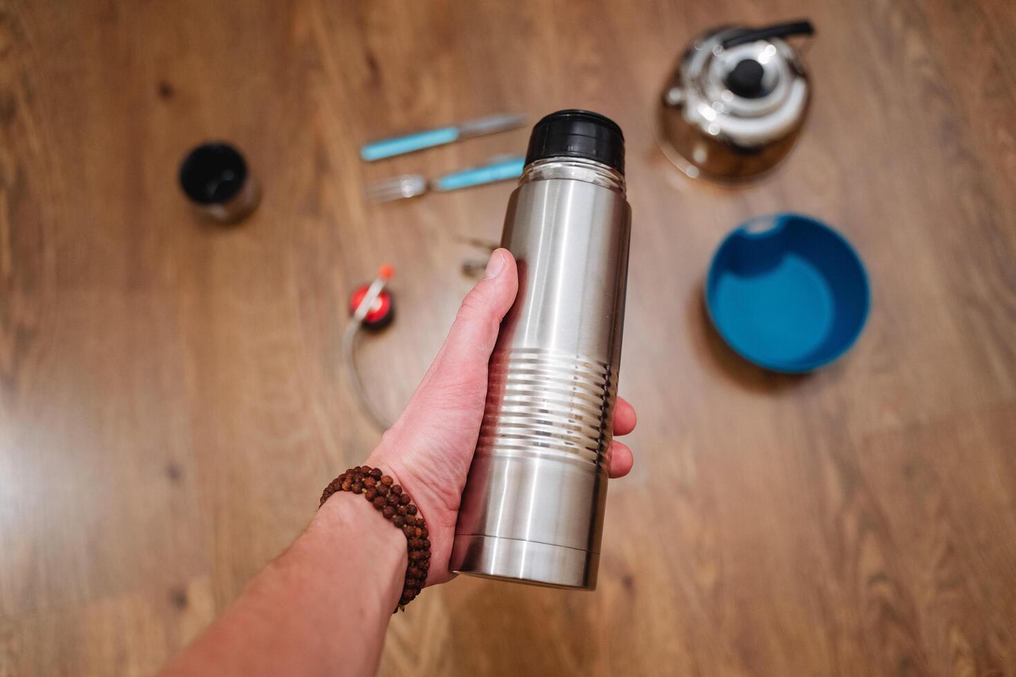 A thermos in his hand is shot close-up. Metal vacuum vessel. Steel bottle. Tea is brewed in a thermos. photo