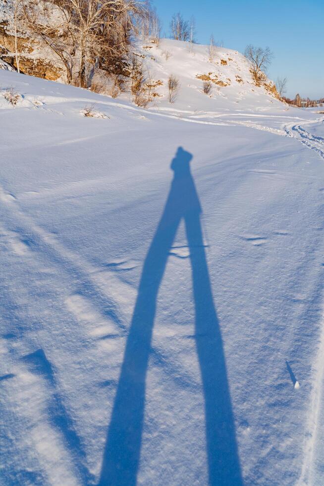 The shadow of a person is displayed on the snow. The landscape, the outline of a person stands on two legs. photo