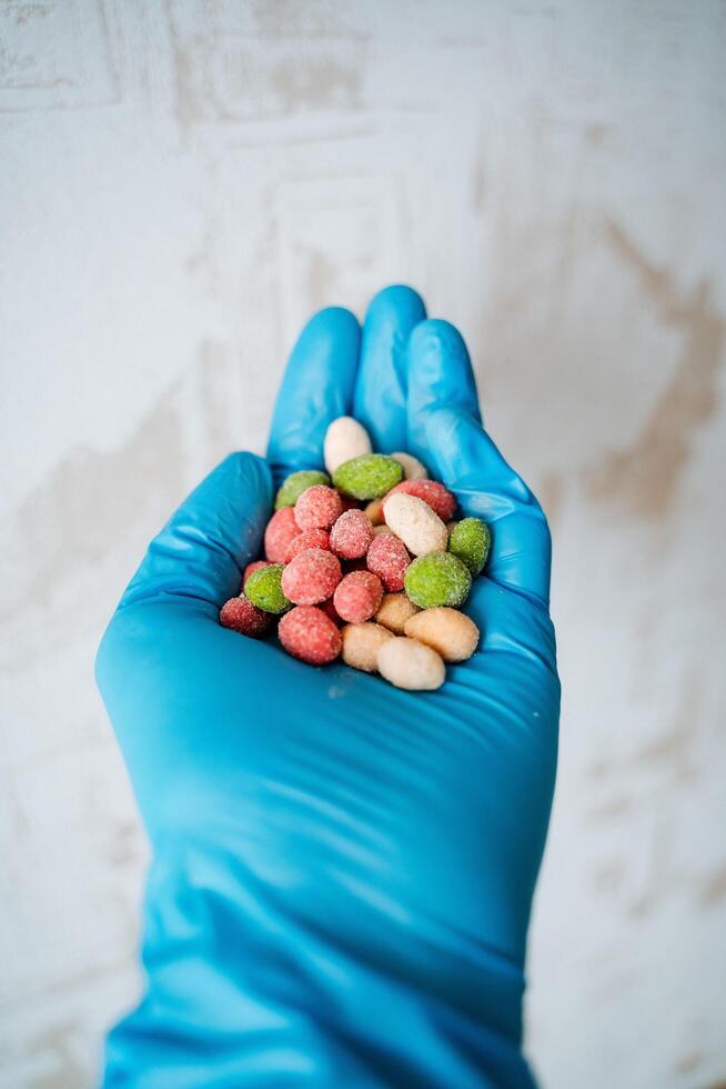 A handful of peanuts colored hand in a glove. Salted nuts are bright in color. The dragee is poured into the hand. Chemical product in a protective glove. photo