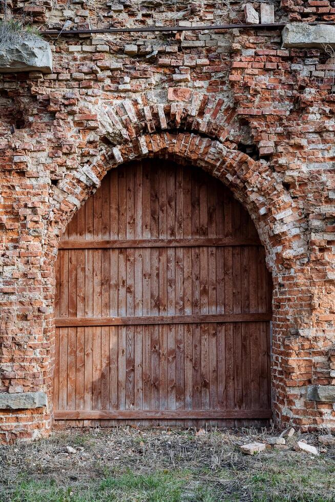 antiguo de madera puerta de rojo color, Entrada a el antiguo estructura, destruido ladrillo, fortaleza fragmento de el puerta, arco en el castillo muro, histórico edificio foto