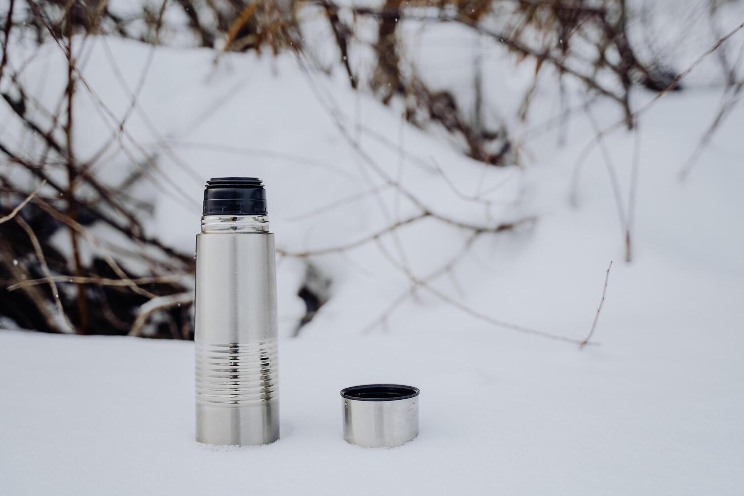 The thermos stands on the snow. Metal dishes vacuum. Hot coffee is brewed in a thermos. Winter cold photo. photo