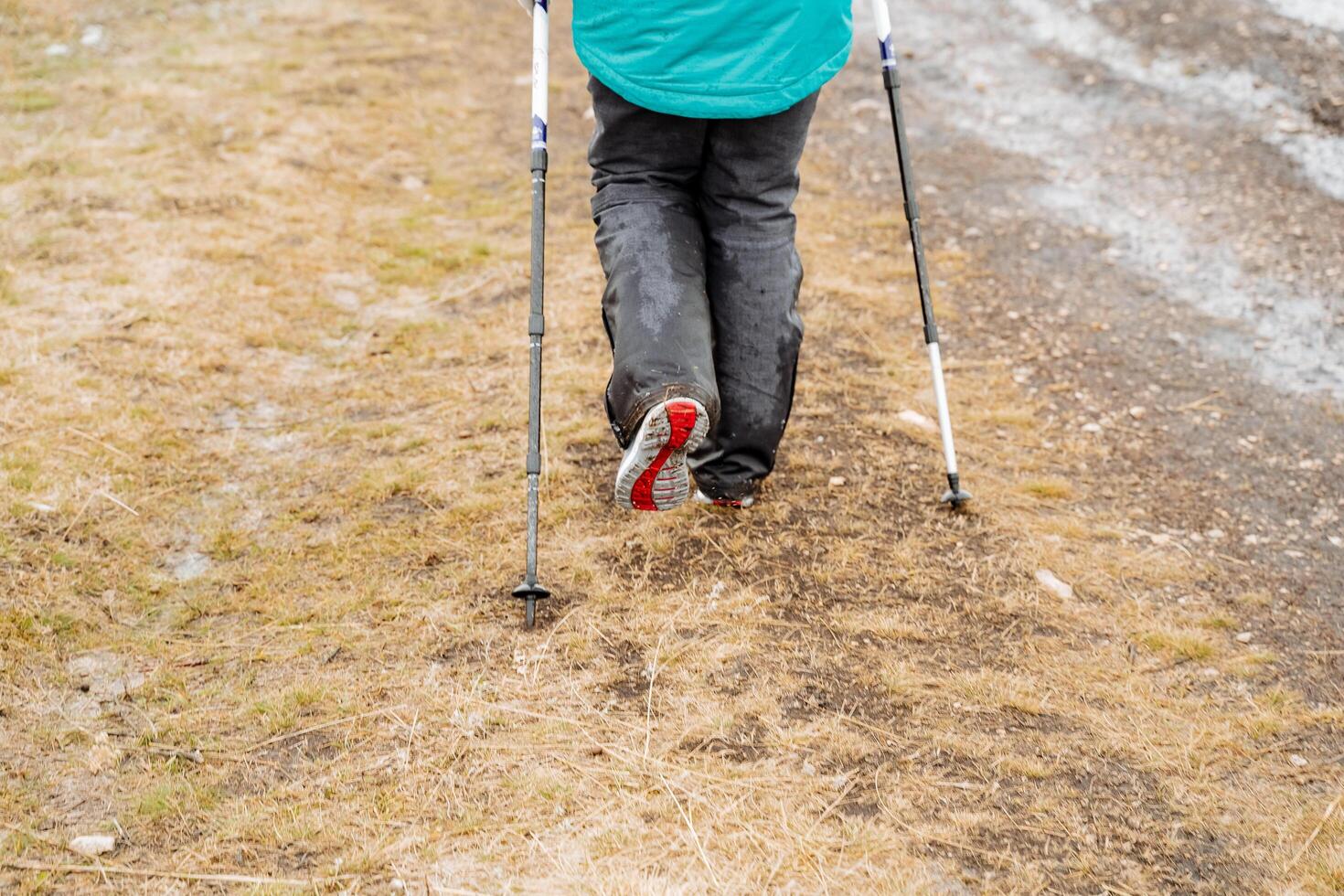 Feet in pants go along the road, Nordic walking, a tourist walks across the field leaning on trekking poles, the sole of a shoe, a walk in the fresh air. photo
