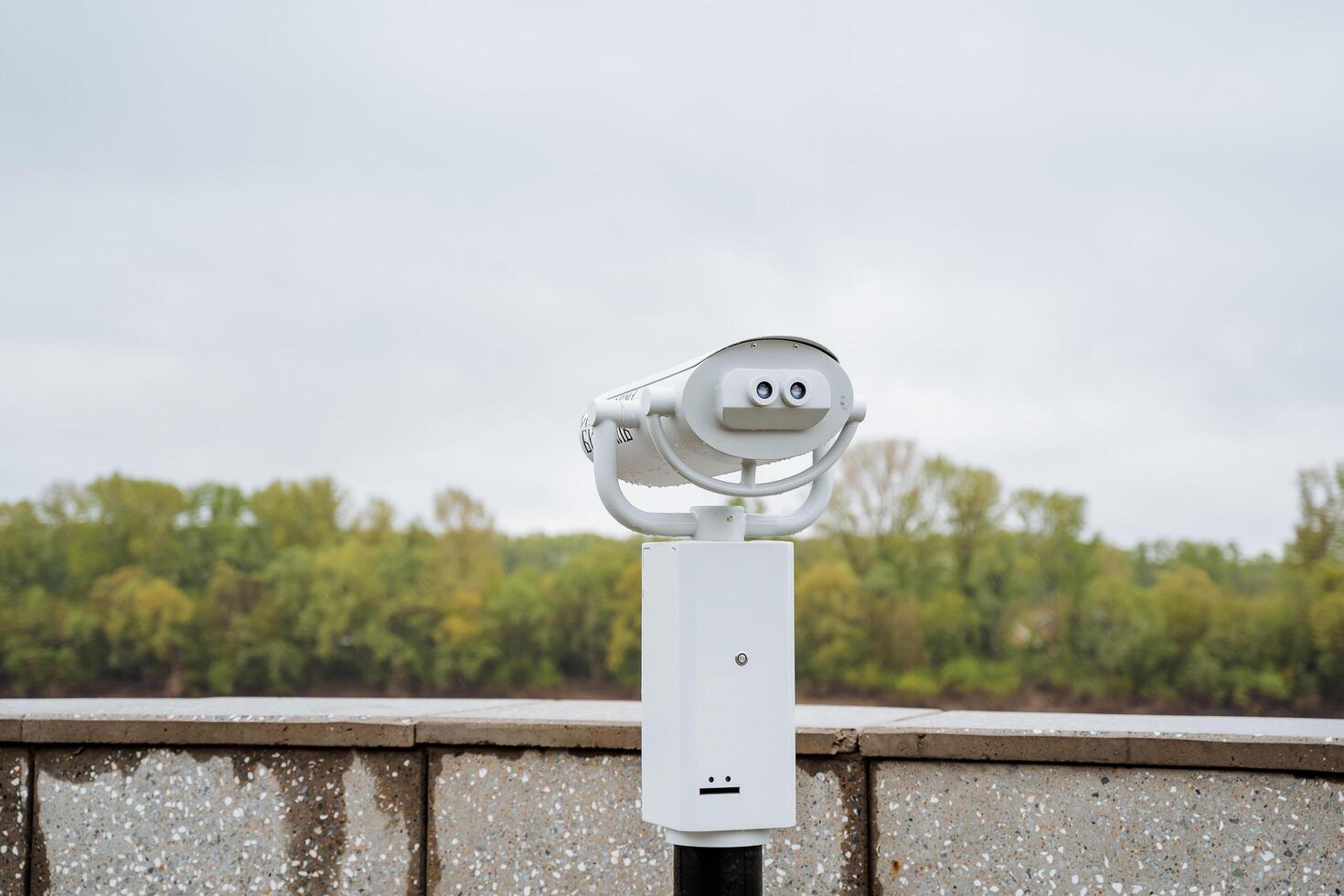 A white street telescope stands in the park, an observation deck on the embankment, long-range binoculars, a panoramic view, an attraction for money, a magnifying glass. photo