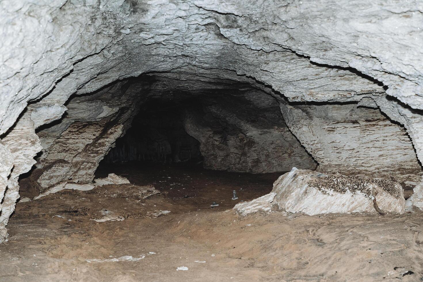 Passage underground in a stone cave, a karst cavity in the mountainside, darkness at the end of the tunnel, clay floor, gray limestone walls. photo