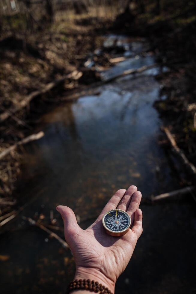 A retro-style compass rests on a person's open palm. A man holds a compass in his hand, orienteering in the forest, a person got lost, a tourist got lost. photo