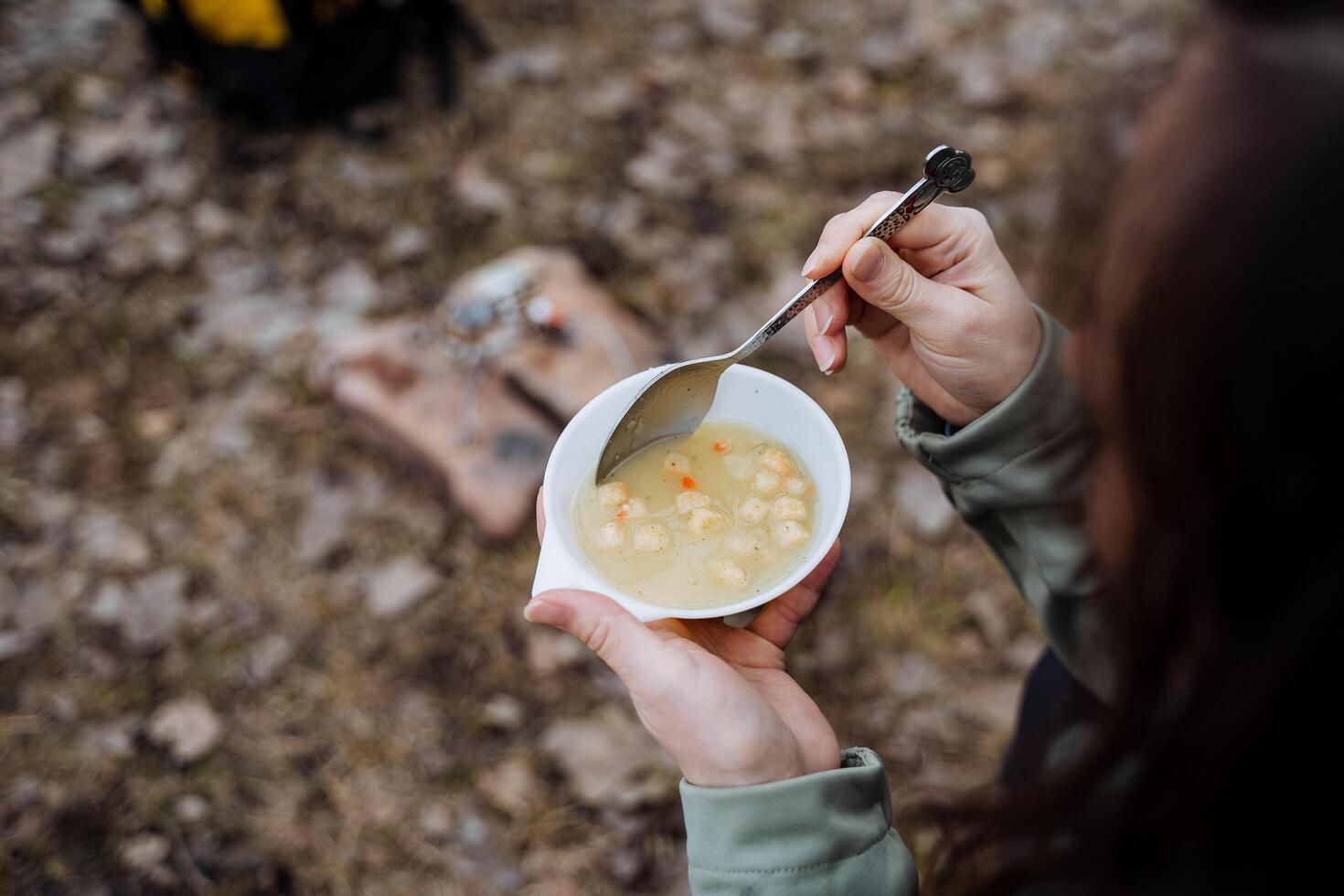 el niña sostiene en su manos un plato de sopa en un caminata en naturaleza, un del turista desayuno, comiendo líquido comida con un cuchara en el bosque, almuerzo en el primavera en el bosque. foto