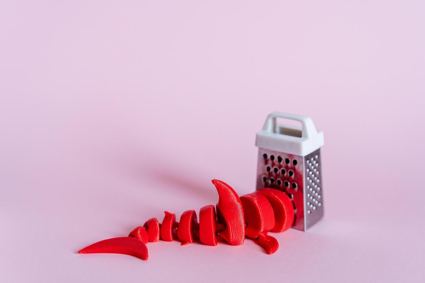 a toy shark and a grater on a pink background. surrealism and abstraction. the tail of a red shark peeks out from the corner. children's toys of small sizes photo