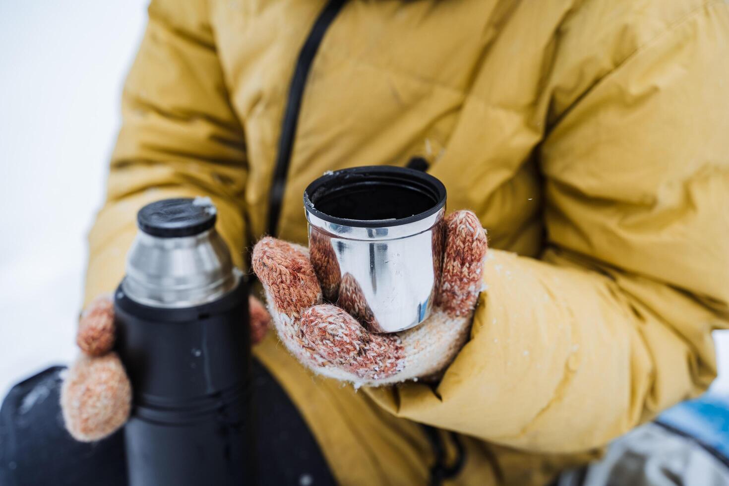 Thermo mug in hand. A hand holds a mug of hot tea. Drink tea in the winter outside. A metal cup with a drink is held by a person. Tea from a thermos. photo