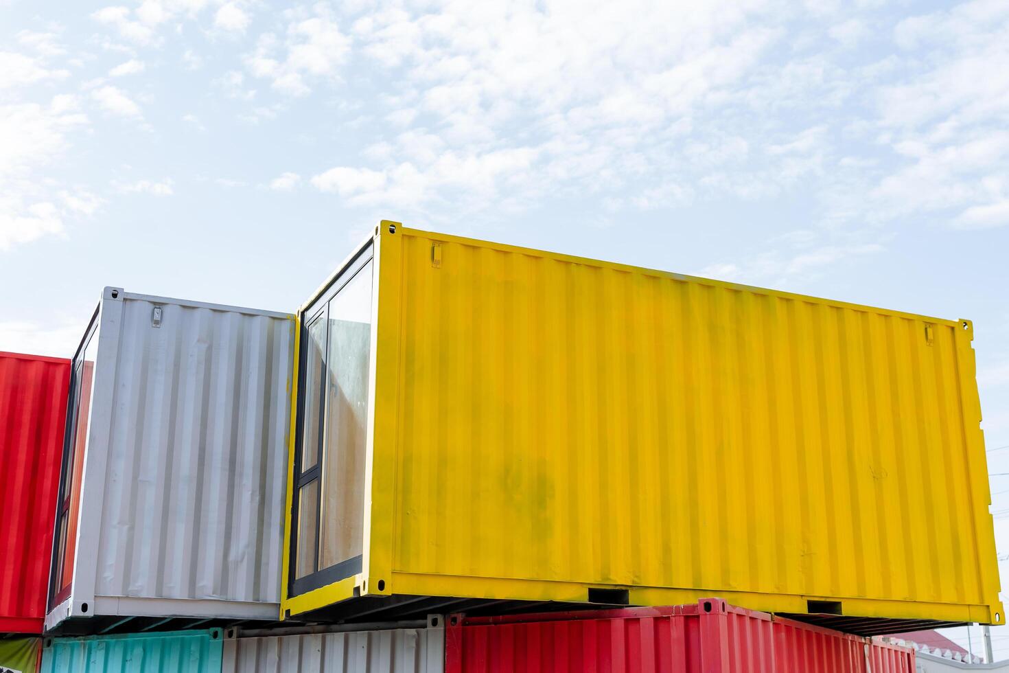 A yellow sea container with a glass wall stands on the roof of the building, a set of colorful containers, durable thick metal, a marine theme, a blue sky. photo