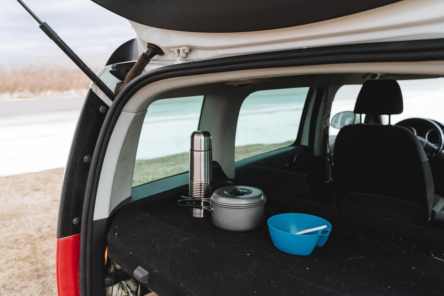 Tourist utensils are in the trunk of the car, lunch in nature, camping in the car, a thermos with tea, a pan with food, a plate with a spoon. A set of dishes for relaxation. photo