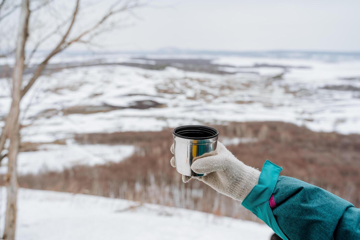 A hand holds a glass of tea against the background of the forest, a mug of hot drink in the hand of a person, drink coffee in winter in nature, the concept of warmth, warm up in the cold season photo