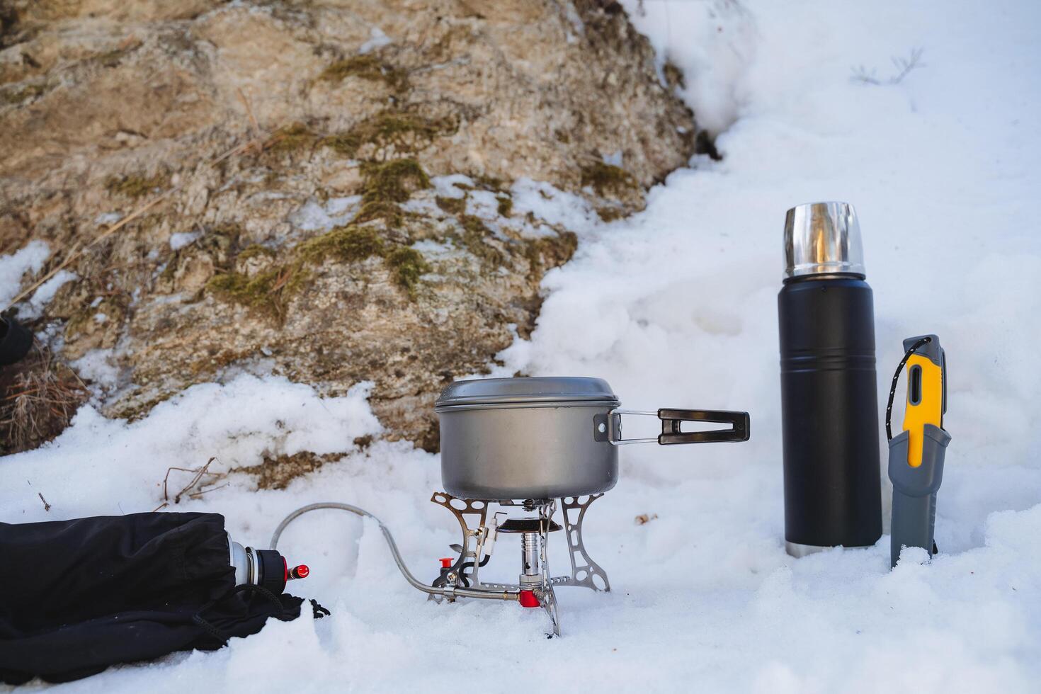 Tourist utensils, cooking in nature in the winter season, a burner with a pan stands on the snow, a thermos with tea, a bushcraft knife. photo