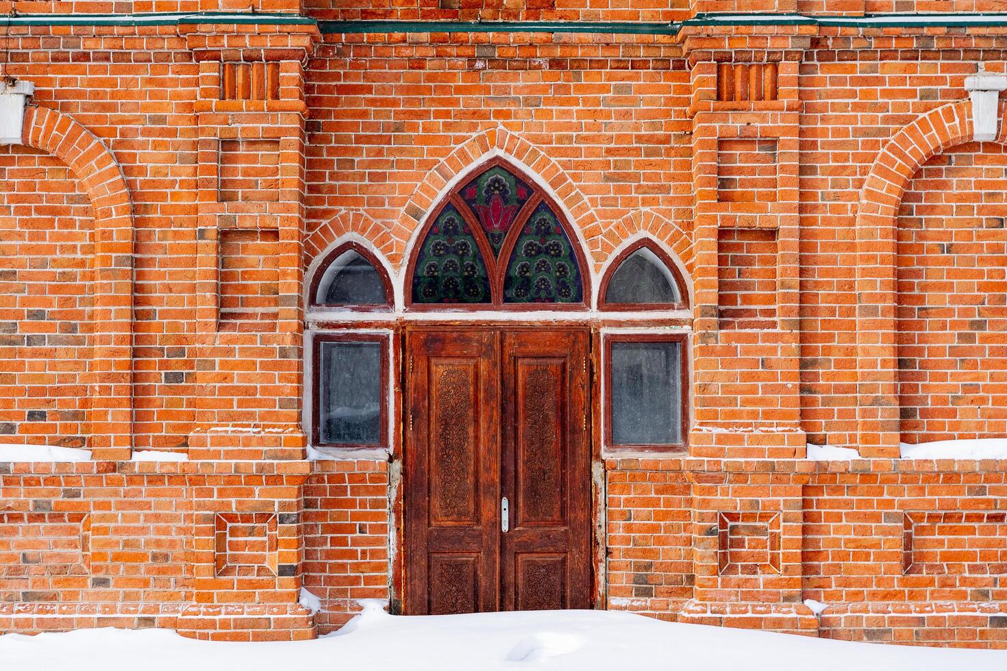 Entrance to a brick building. Arched windows and doors. Heavy wooden door and stained glass windows. Snowdrifts in front of the entrance photo
