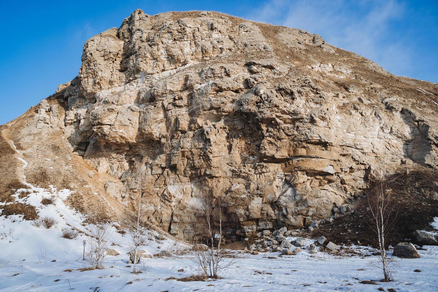 Rock entrance to the cave Karlamanskaya Russia Southern Urals Bashkortostan, winter landscape, spring in the forest the sun warms, warm weather, blue sky photo