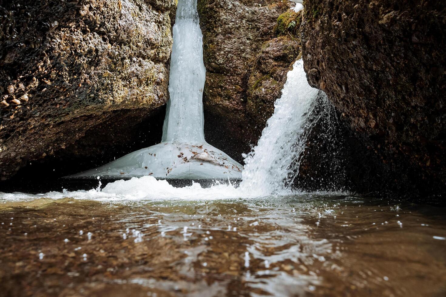 A waterfall falls on the side of the cliff, ice hangs over the water, an underground cave with a waterfall, a spring flood in the mountains, an underground lake. photo
