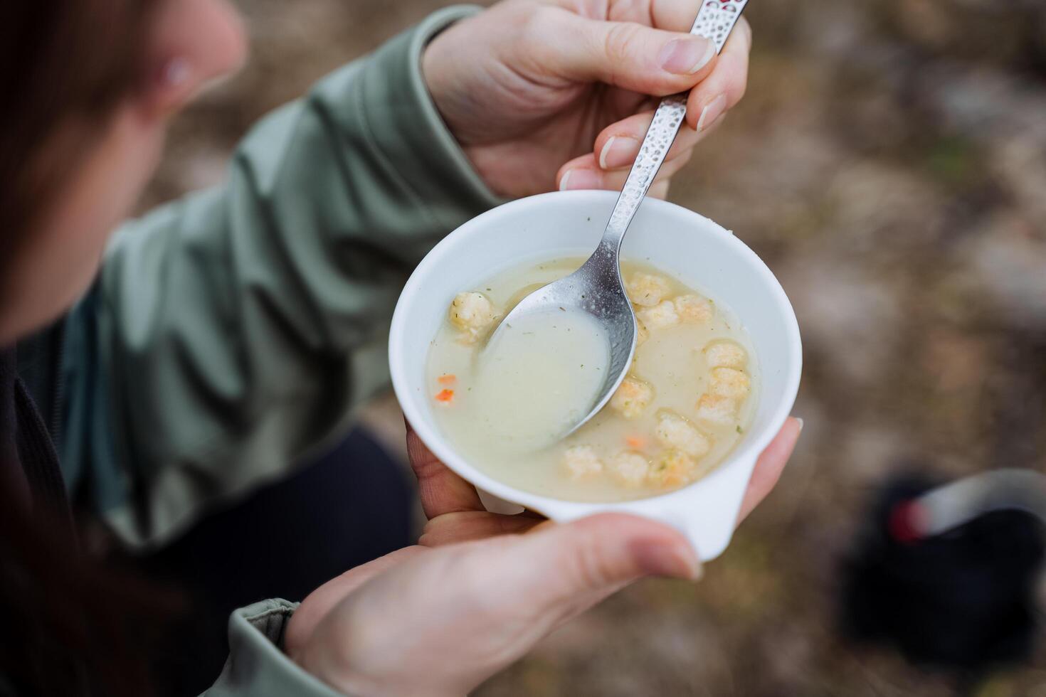 There is soup with a spoon, a plate of food shot close-up, the concept of tourist food on a hike, an instant lunch, croutons floating in the soup. photo