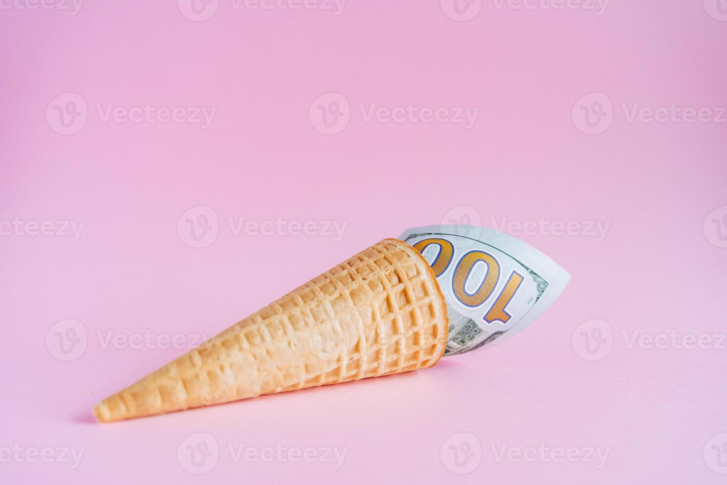 A hundred dollars in an ice cream cone. Unusual ice cream with a bill. A horn with money on a pink background. Interesting and abstract subject shooting photo
