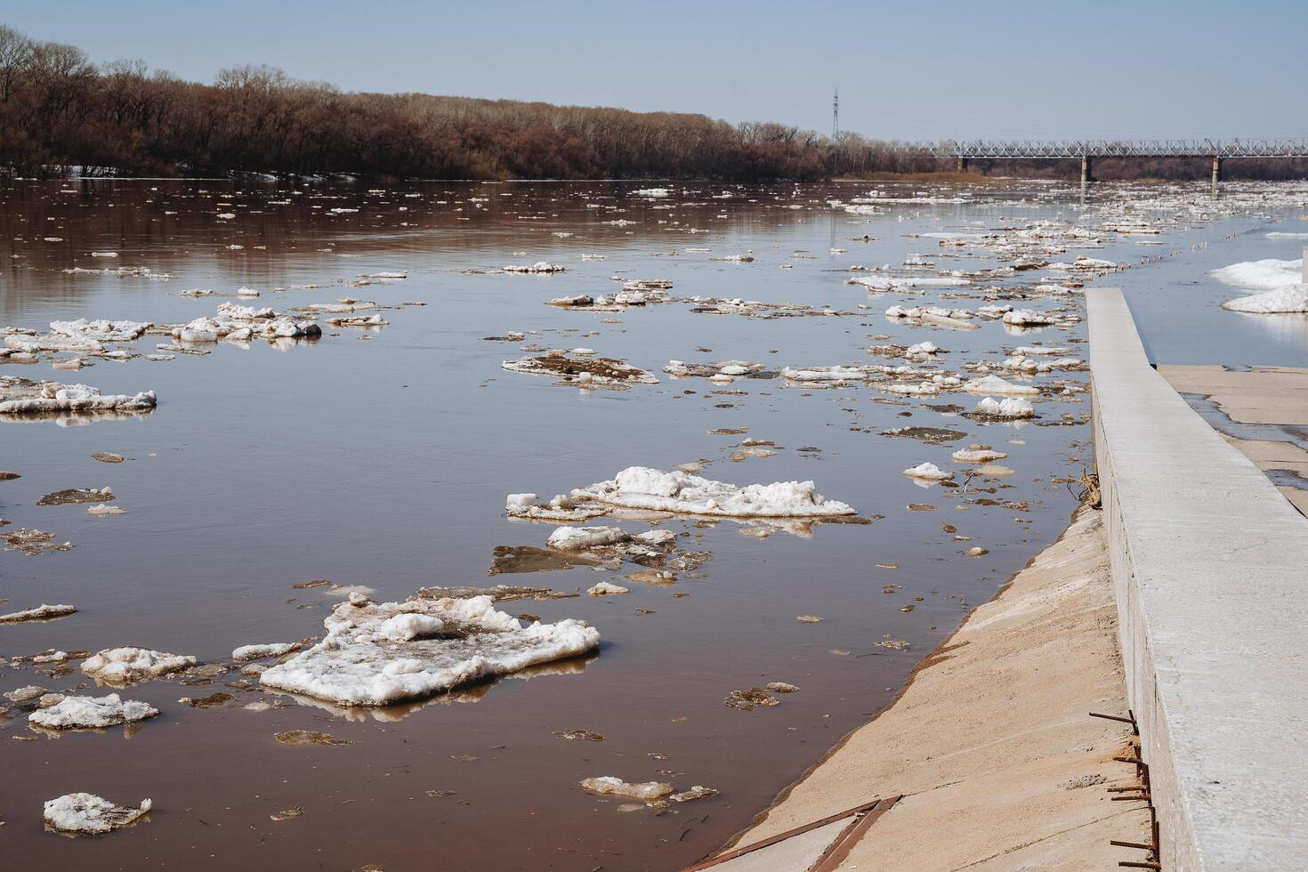 Spring flooding on the river float pieces of ice, ice on the water, concrete embankment, dirty water, snow melted, flooding. photo