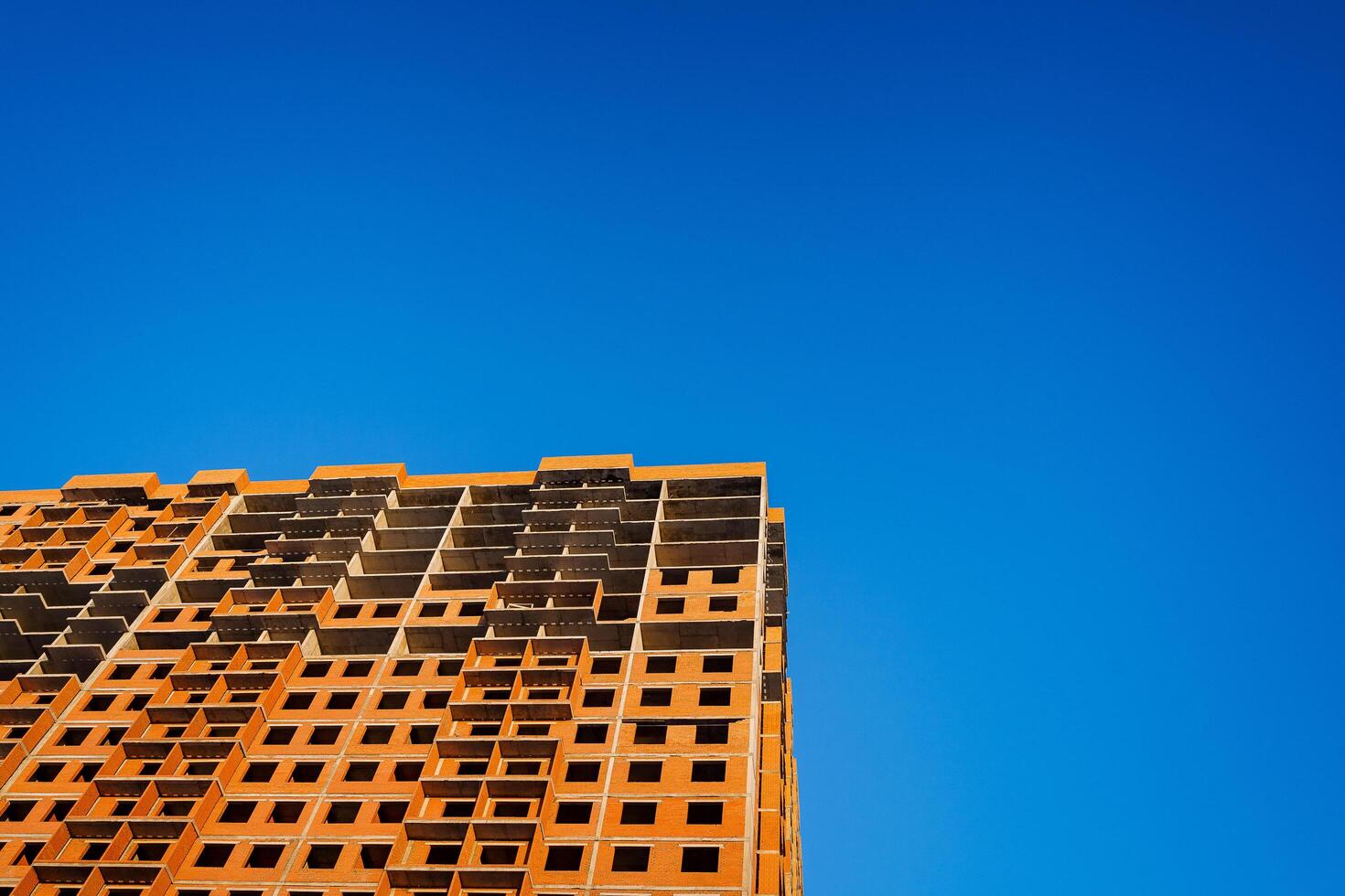 A piece of the building is under construction. The walls of the house are lined with red brick. An unfinished building against a blue sky. photo