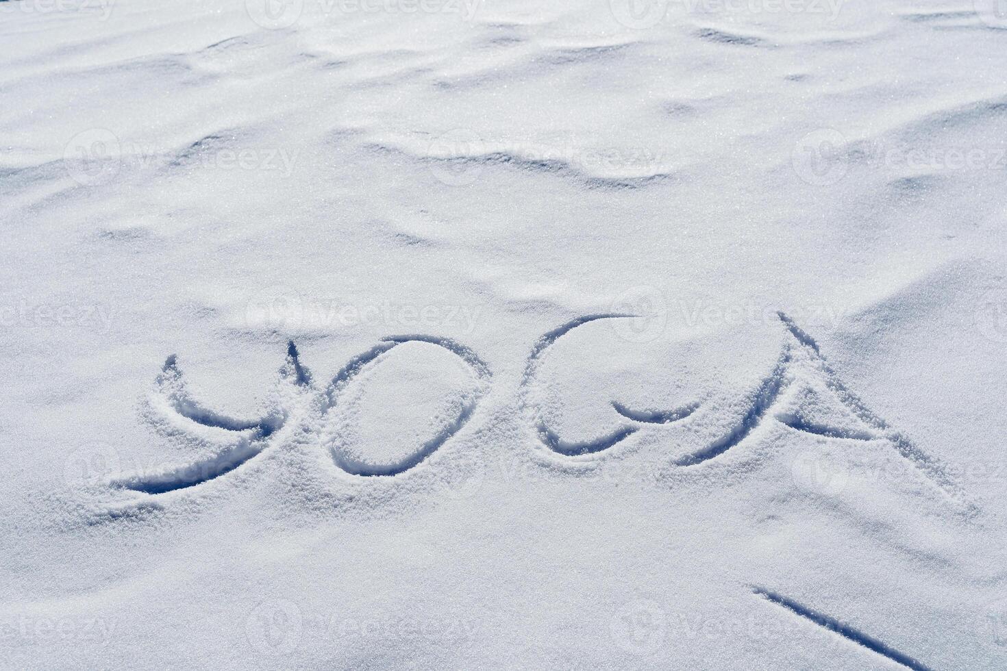 Yoga text is written on white snow in winter, the texture of the background is frozen letters, the symbol of Zen meditation, silence in nature. photo