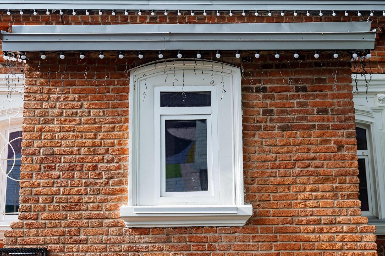 An old-style brick house, a window in the wall of the house, a white window, the facade of the building in Evprope, a historical landmark, roof lighting. photo