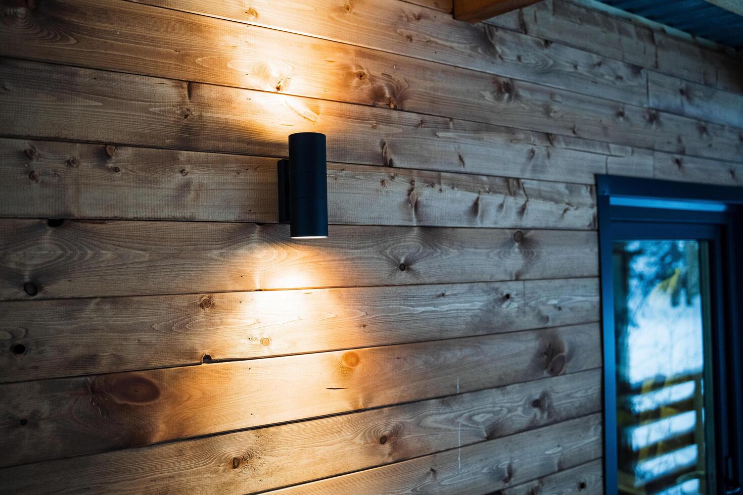 Bright street lamp with double light. Lighting on the streets near the house. Wooden walls of the house. High-quality and good construction and repair photo